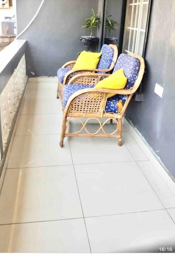 Un balcon avec deux fauteuils en osier, chacun agrémenté d’un coussin jaune, et une plante en pot en arrière-plan.