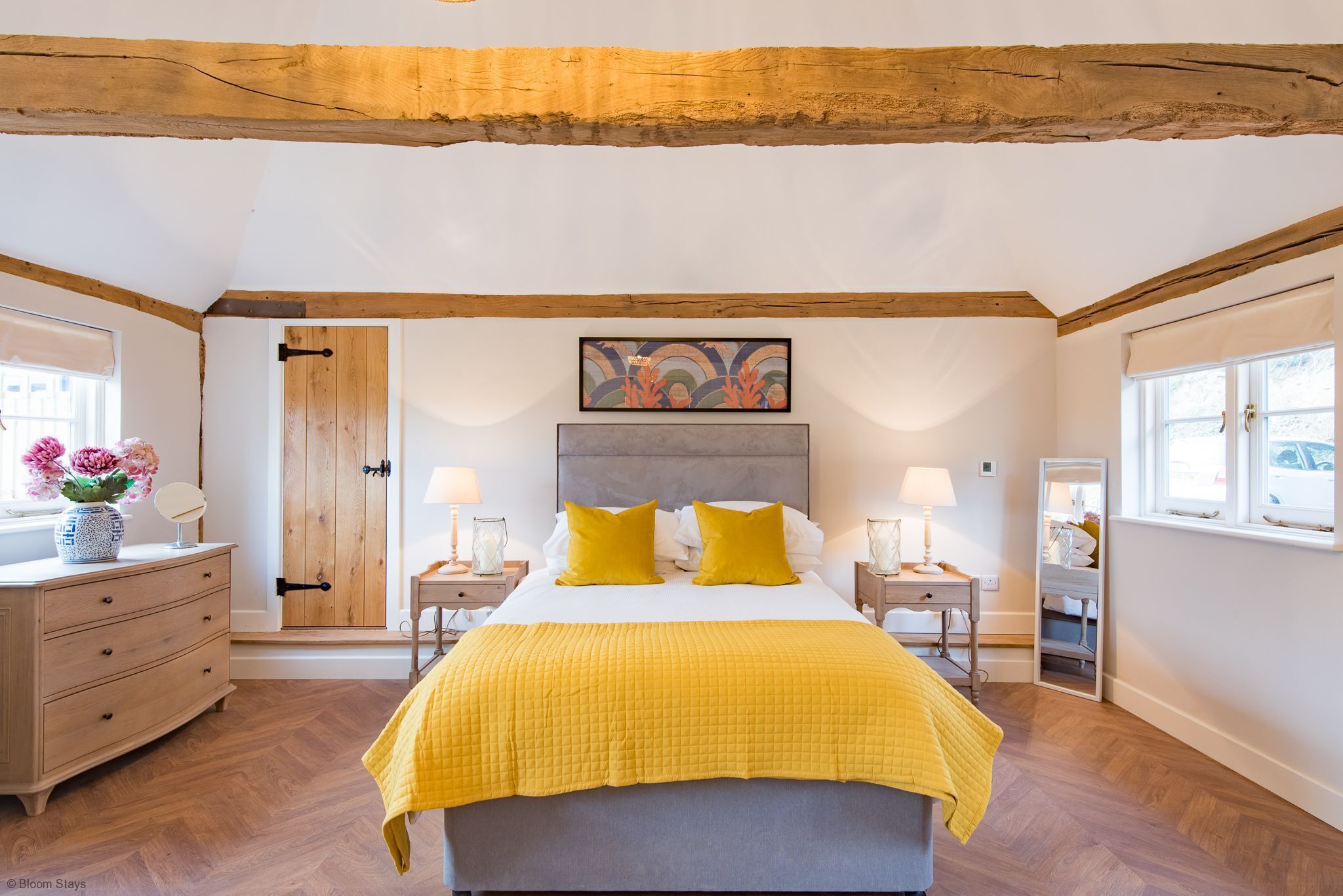 A bedroom with a bed, wooden headboard, bedside tables, lamps, a dresser, and a door.