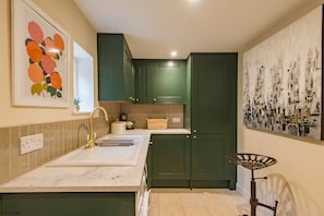 Cozinha com pia, armários verdes, um objeto decorativo na parede e uma cesta de vime sobre o balcão.