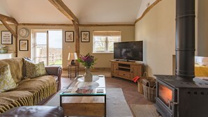 A cozy living room with a leather sofa, a glass coffee table, a TV, a fireplace, and wooden beams on the ceiling.