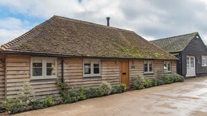 A wooden cottage with a tiled roof, a front door, and a small garden area with various plants.