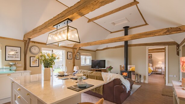 A spacious living area with a large wooden beam ceiling, a central island with a marble countertop, a comfortable sofa, and a television.