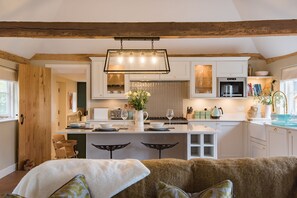 Una cocina moderna con una isla central, vigas de madera y una lámpara colgante.