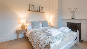 A bedroom with a bed, bedside lamps, a shelf with pictures, and a fireplace. - Wow, wow! Amazing immaculate period house and hot tub by Bloom Stays - discounts available (Faversham)
