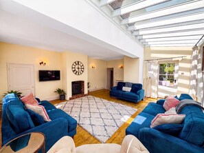 A spacious living room with a large blue sofa set, a flat-screen TV, a fireplace, and a large window with curtains.