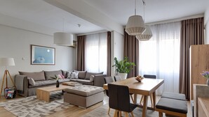 Un salon moderne comprenant un canapé, un pouf, une table basse, une table à manger, des chaises et une plante en pot.