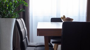 Un coin repas comprenant une table, des chaises, une plante en pot et une fenêtre avec des rideaux.