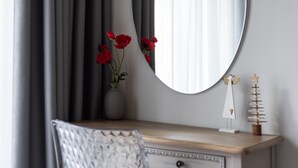 Une commode en bois avec un miroir, un vase rempli de fleurs rouges et une petite statuette d’ange.