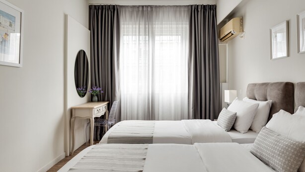 Une chambre d’hôtel avec deux lits, un bureau, une chaise, un miroir et une fenêtre avec des rideaux.