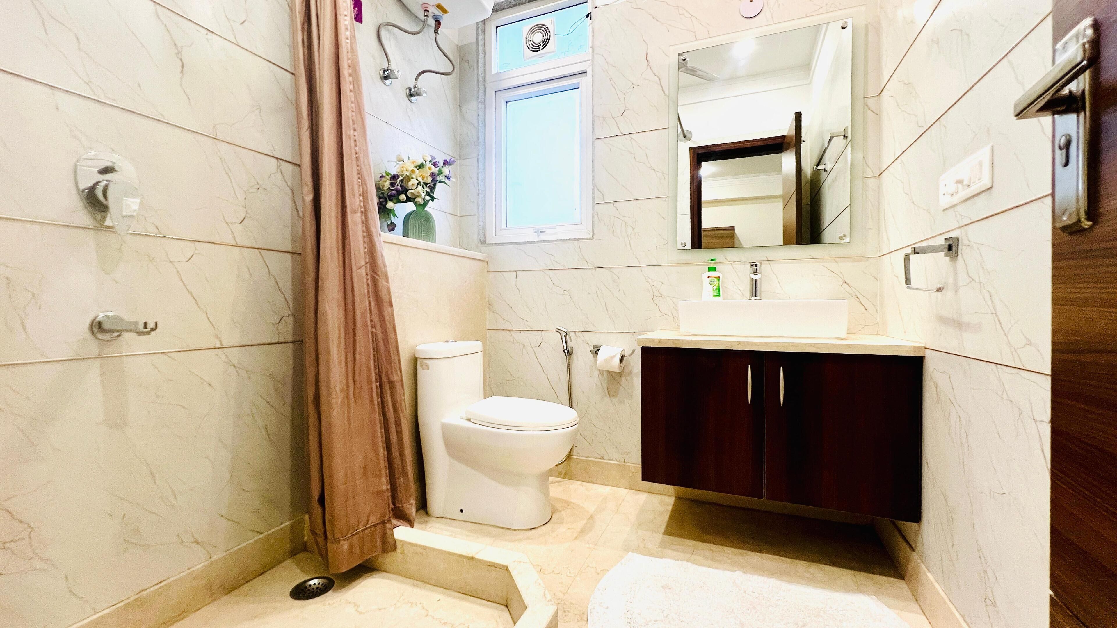 A bathroom with a toilet, sink, mirror, shower curtain, and marble tiles.