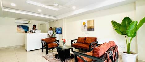 A modern reception area with a desk, chairs, and a large potted plant.
