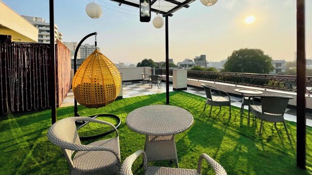A rooftop terrace with outdoor seating, a hanging chair, and a view of the city skyline. - Olive Service Apartment-Golf Course Road (Gurugram)
