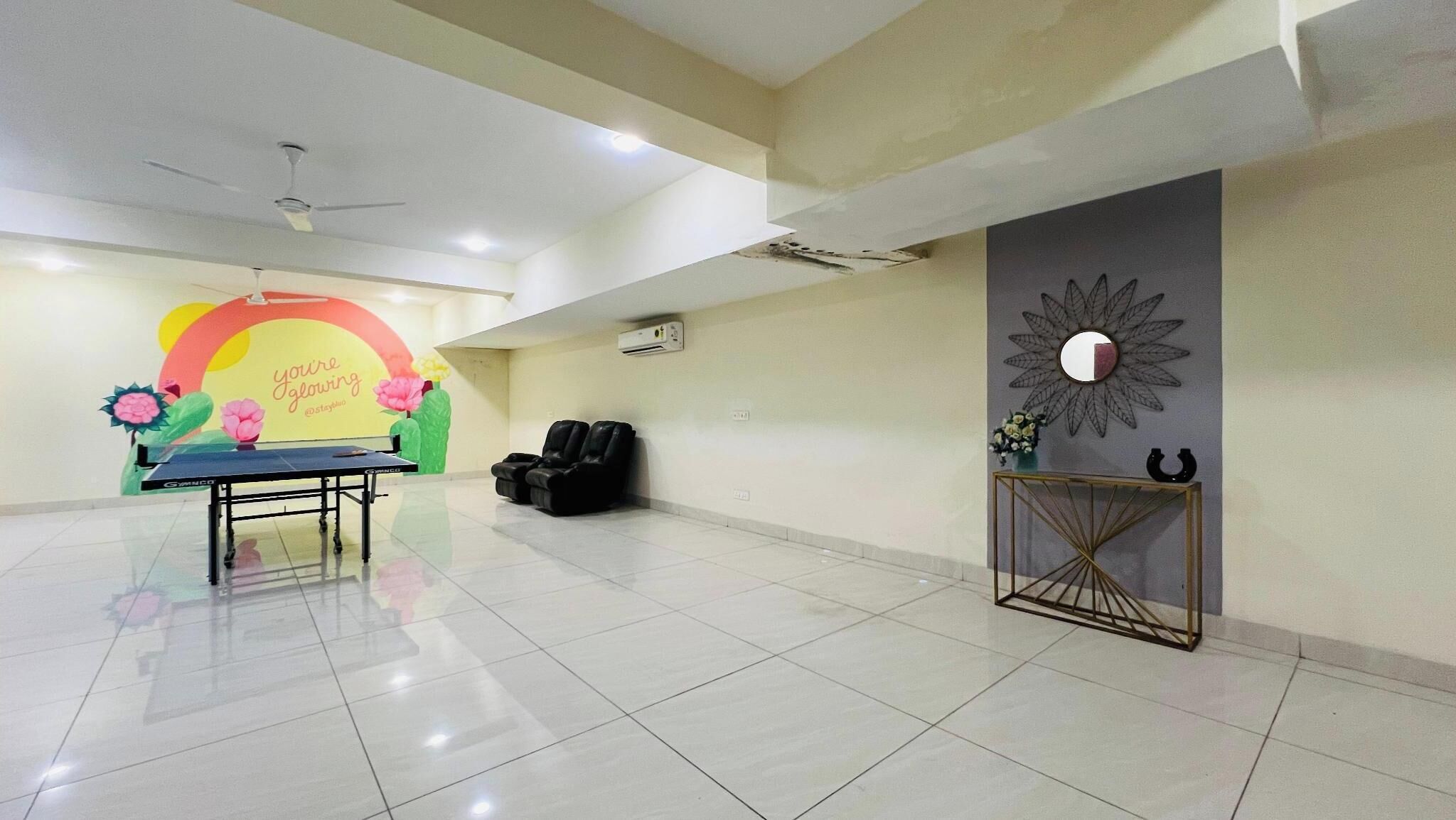A spacious room with a ping pong table, black leather chairs, a decorative wall with a sun motif, and a console table with a vase.
