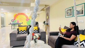 A modern living room with a grey sofa, a small coffee table with a vase of flowers, and a wall with framed pictures and a decorative mirror. - Olive Service Apartment-Golf Course Road (Gurugram)