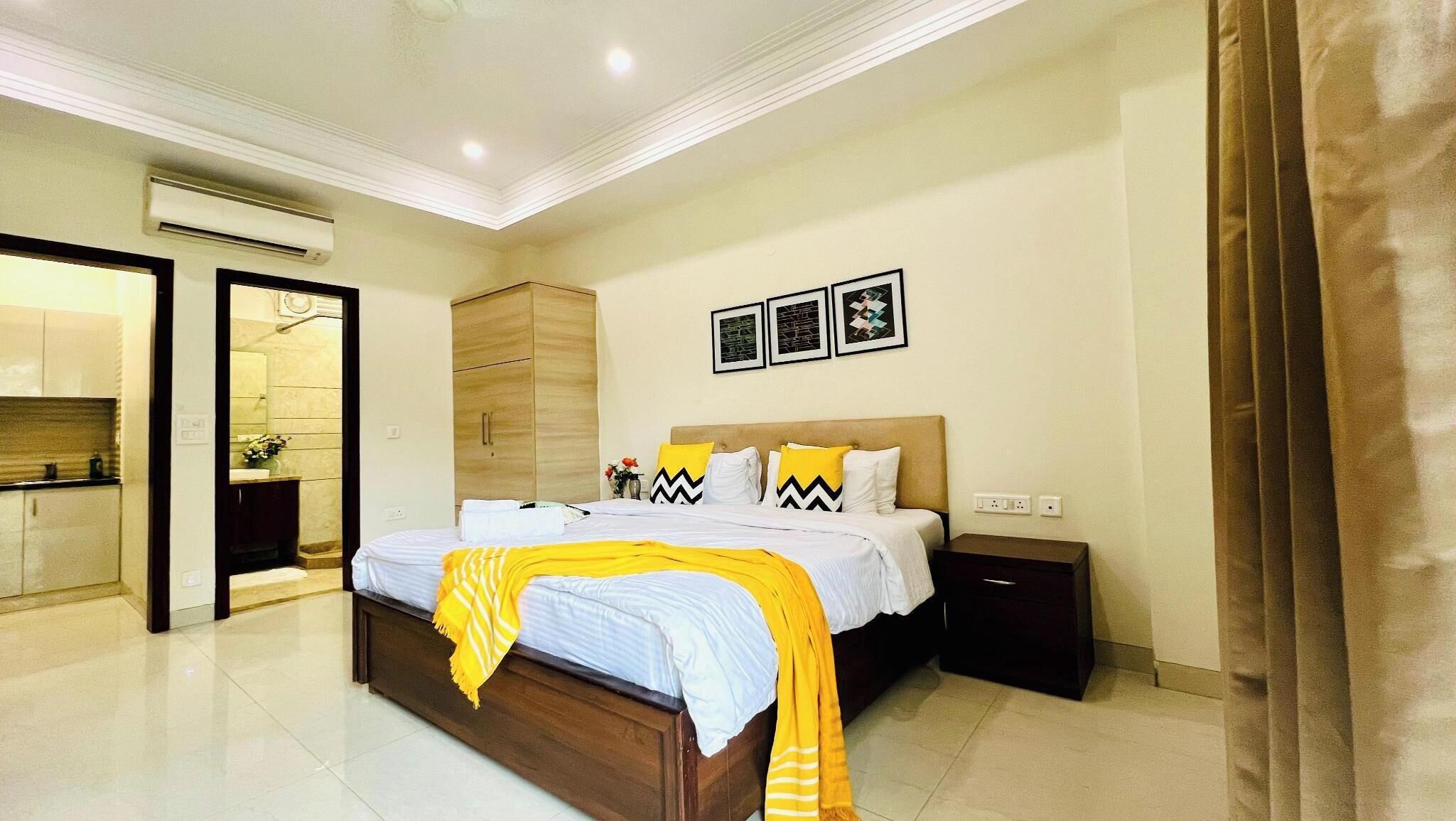 A modern bedroom with a large bed, a wooden wardrobe, a bedside table, and a bathroom visible through an open door.