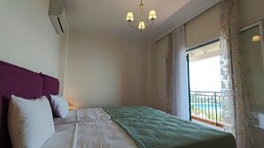 Hotellihuone, jossa on sänky, kattokruunu, ilmastointilaite, parveke, jolta on näkymä, ja ikkuna, jossa on verhot.