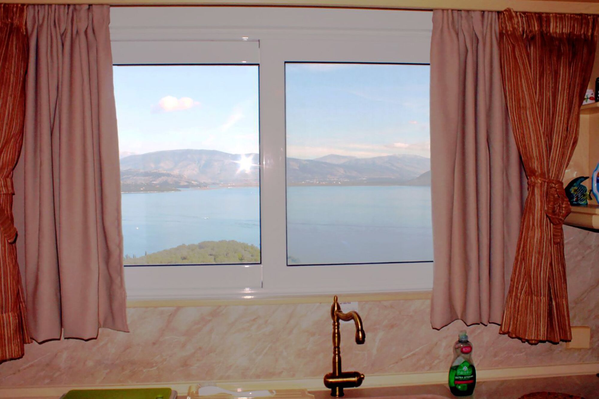 A bathroom with a window overlooking a lake and mountains, a sink with a faucet, and a bottle of soap on the counter.