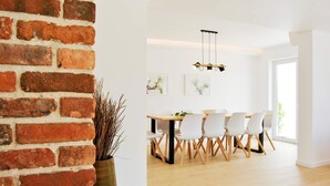A dining area with a brick wall, a wooden table, white chairs, and a hanging light fixture.