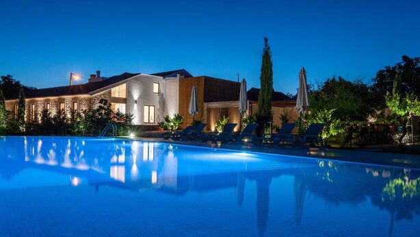 A modern hotel with a swimming pool, lounge chairs, and a well-lit outdoor area at dusk.