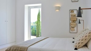 A bedroom with a bed, a bedside lamp, a window, and a wall-mounted light fixture.
