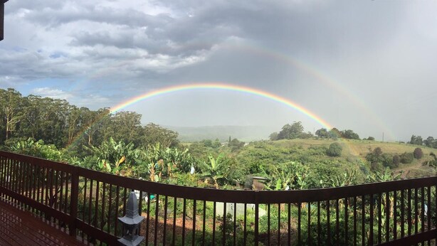 Eine Holzterrasse mit Geländer, die auf eine üppige Landschaft mit Regenbogen blickt.