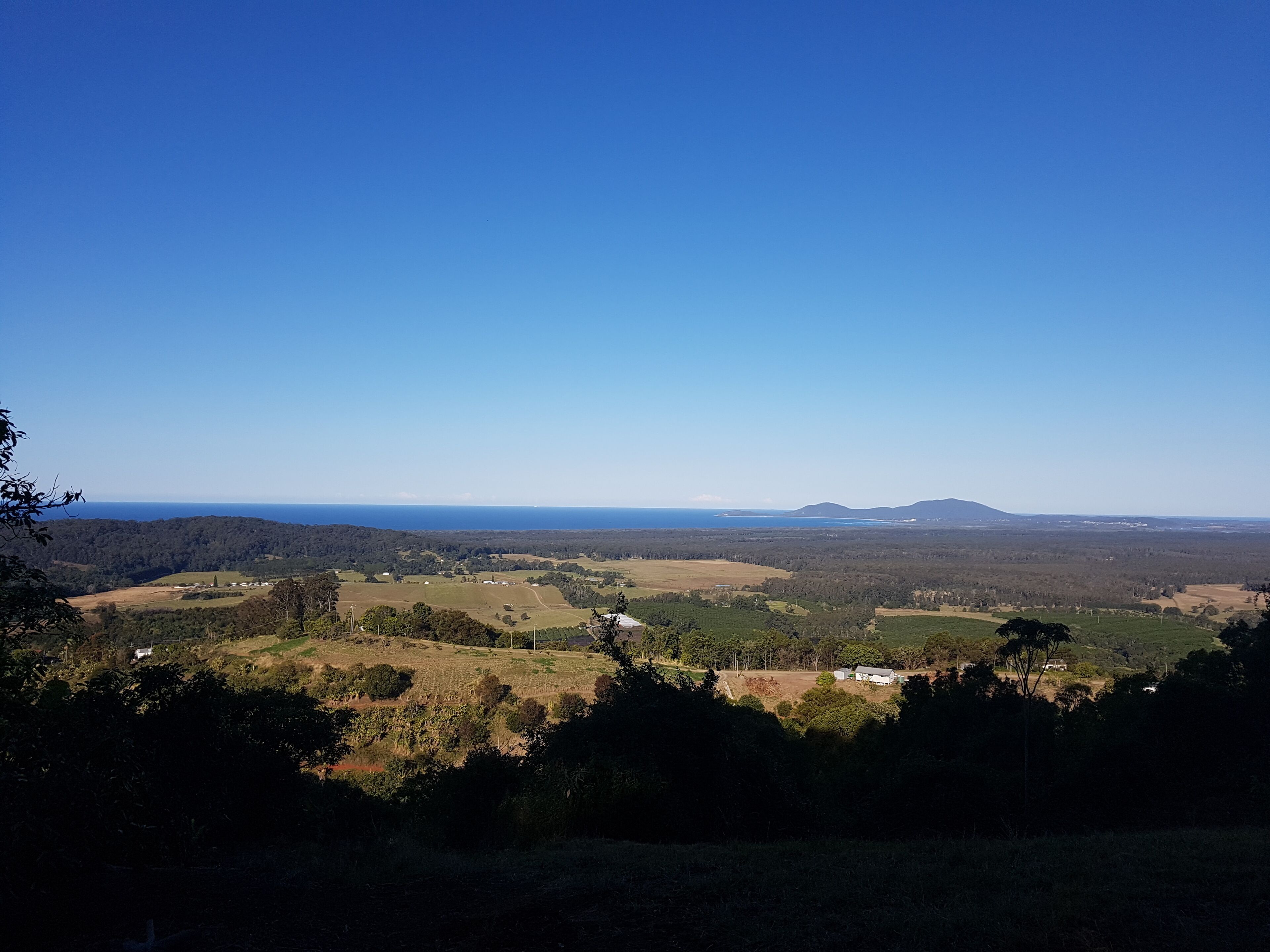 A panoramic view of a rural landscape with rolling hills, a distant mountain, and a clear blue sky.