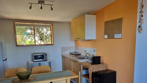 Eine kompakte Küche mit Mikrowelle, Spüle und kleinem Backofen. Ein Esstisch mit Stühlen und ein Fenster sorgen für natürliches Licht.