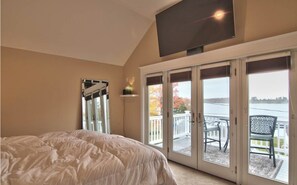 Relax in this serene bedroom with a large bed and a flat-screen TV, offering a view of the water and surrounding foliage through the sliding glass door.