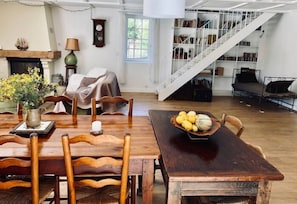 Ein geräumiges Wohnzimmer mit Esstisch aus Holz, Kamin und Treppe zu einer oberen Ebene mit Bücherregalen.