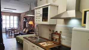 Una cocina con armarios blancos, estufa y microondas. Hay una zona de comedor con mesa y sillas.