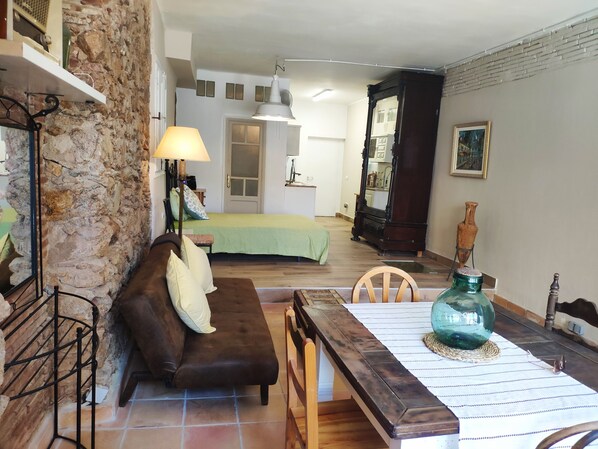 Una habitación acogedora con pared de piedra, un sofá marrón, una mesa de comedor de madera y una cama con estampado de cuadros verdes.