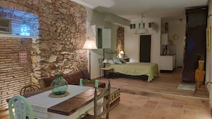 Una habitación acogedora con pared de piedra, una cama, una mesa de comedor con sillas y una pequeña cocina.