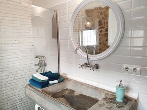 Un baño con pared de ladrillo blanco, un espejo redondo, un lavamanos con grifo y un perchero para toallas.