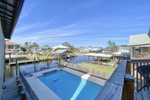 Une piscine avec une terrasse en bois, une vue sur un quartier résidentiel et un ciel bleu dégagé.