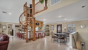 Una cocina amplia con una escalera espiral de madera, un comedor con sillas de metal y un sofá de cuero rojo.