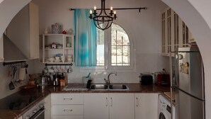 Une cuisine avec une porte en arc de cercle, un lustre, un évier, une cuisinière et un lave-linge.