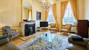 A spacious living room with a fireplace, leather sofas, a glass coffee table, and a large window with curtains. - Le Château des Comtesses (Montignies-sur-Roc)