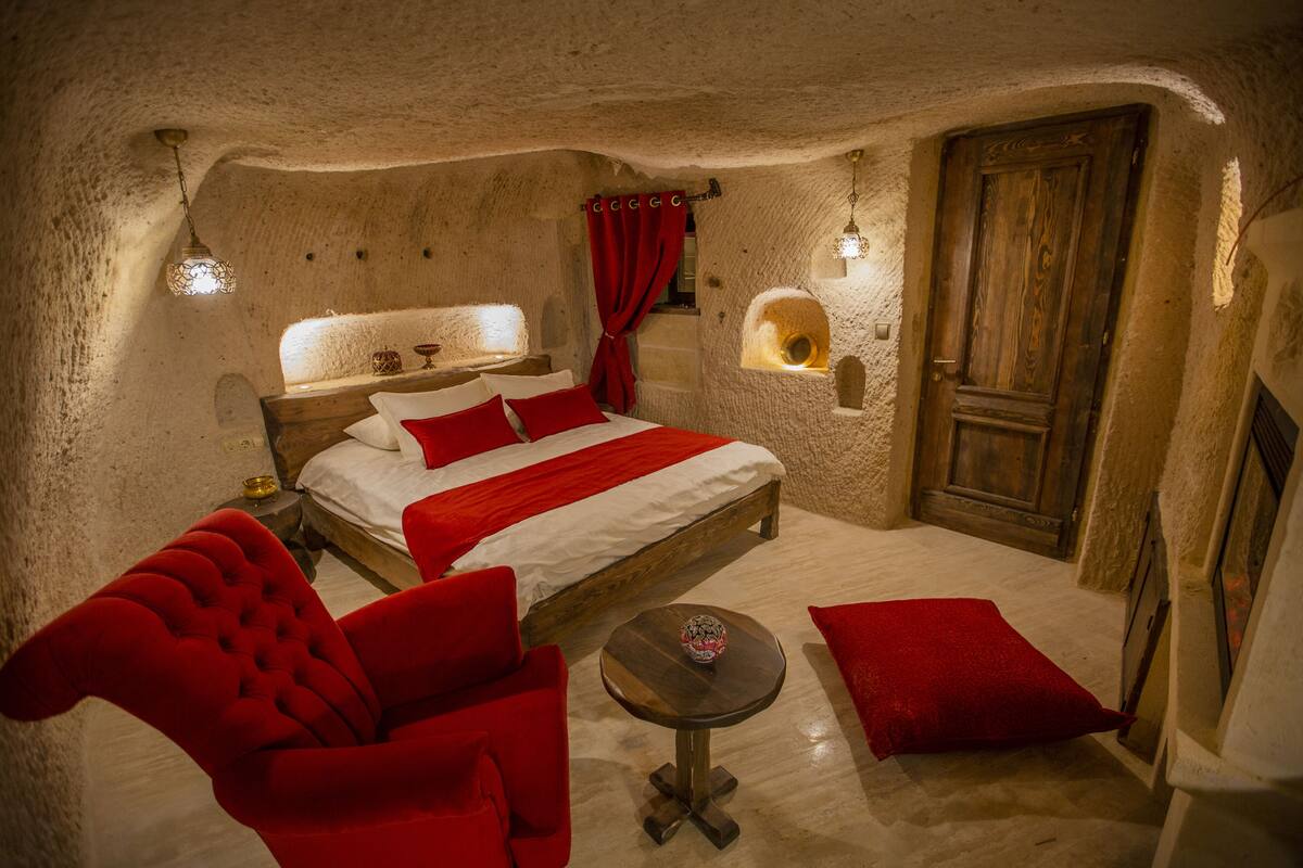 Um quarto aconchegante com uma cama, uma cadeira vermelha, uma mesinha e uma porta de madeira.