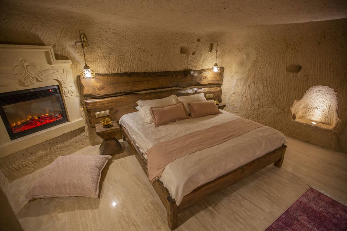 Quarto aconchegante com cama de madeira, lareira e parede texturizada.