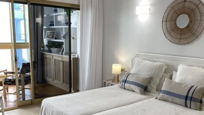 Une chambre avec deux lits, une table de chevet avec une lampe, un luminaire circulaire fixé au mur et une porte-fenêtre coulissante donnant sur un balcon.