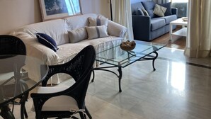 Un salon moderne avec un canapé, une table basse en verre et un fauteuil en osier.