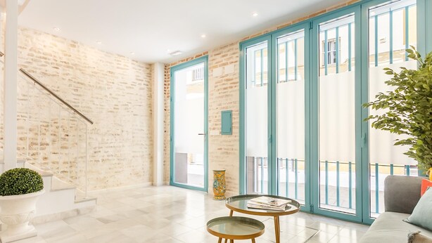 A spacious living area with a staircase, a sofa, two small tables, and a large window with blue frames.
