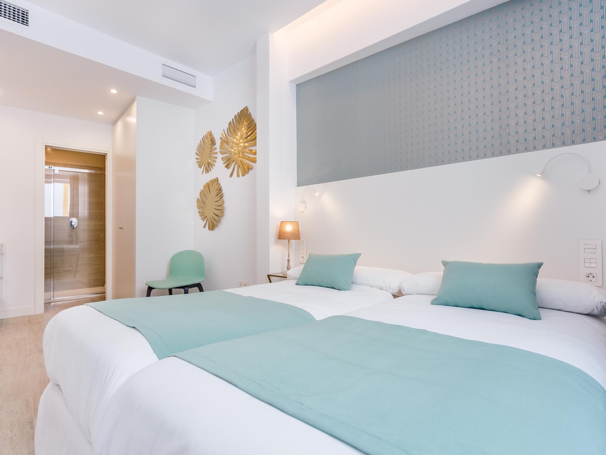 A hotel room with two beds, a green chair, and a decorative wall panel.