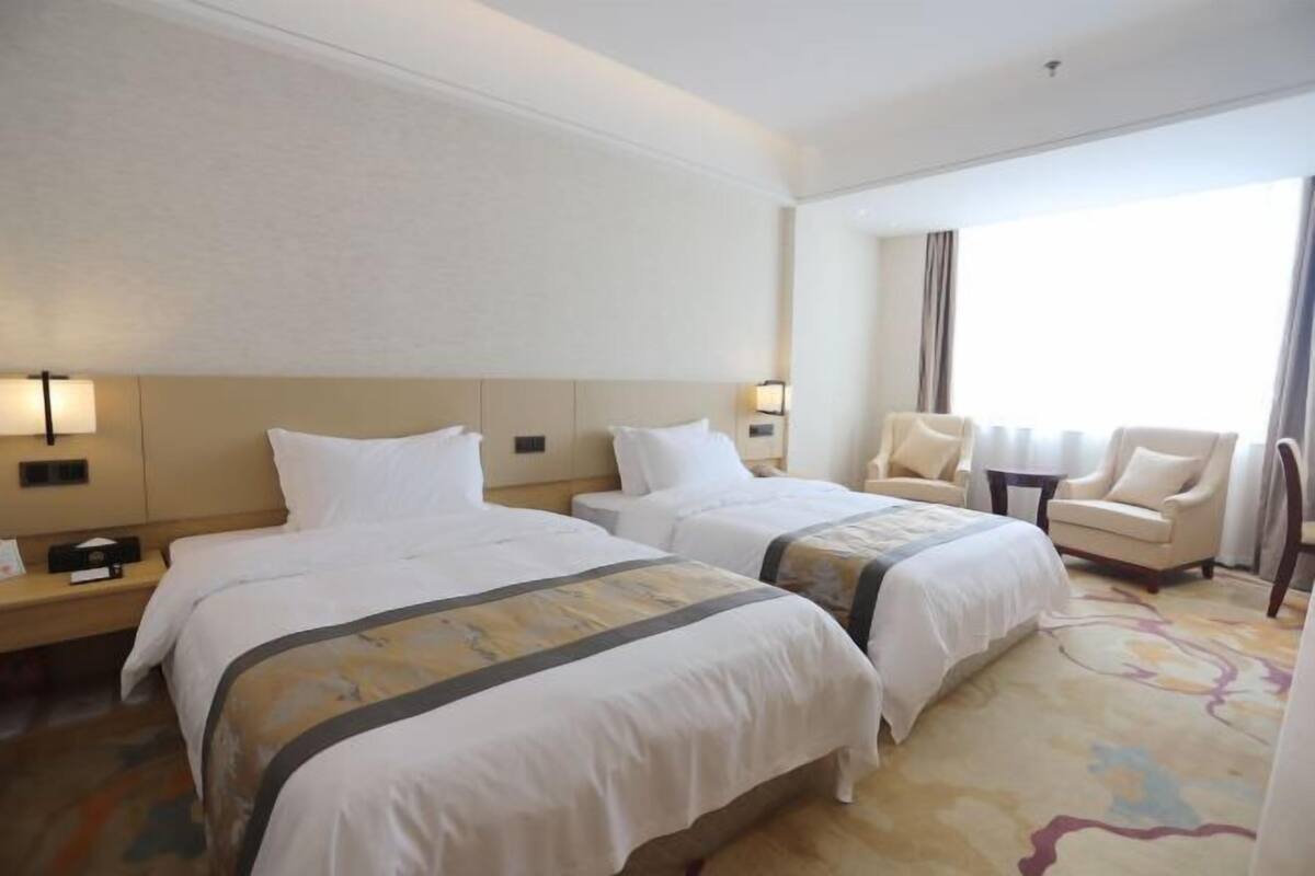 Een hotelkamer met twee bedden, een slaapbank, een tafeltje en een groot raam.