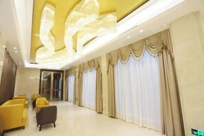 A hotel lobby with a reception desk, seating area, and large windows with curtains. - Nanxiong Guest House (Nanxiong)