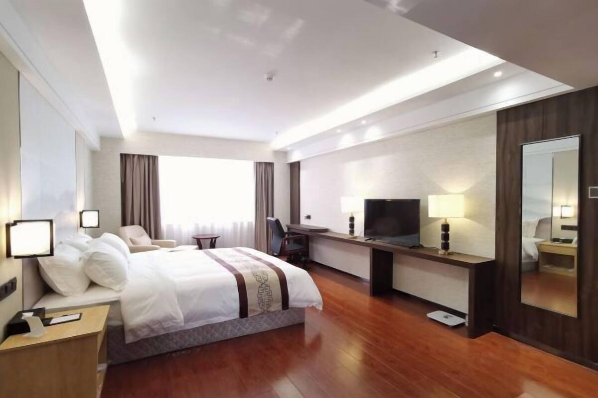 Een hotelkamer met een bed, bureau, televisie en een grote spiegel.