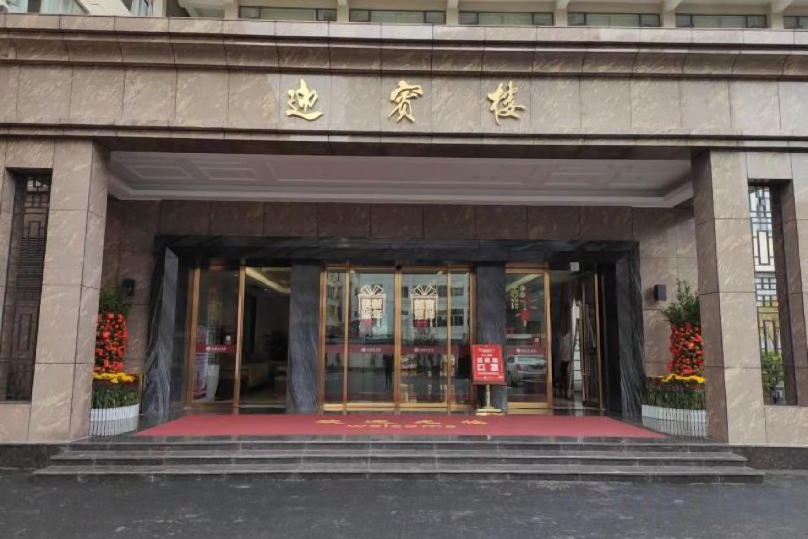 A hotel entrance with a red carpet, glass doors, and a sign above the entrance.