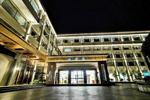 Entrada de un hotel de varios pisos con fachada de vidrio y suelo mojado.