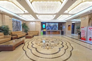 Um saguão de hotel com balcão de recepção, sofás e um padrão decorativo no chão.