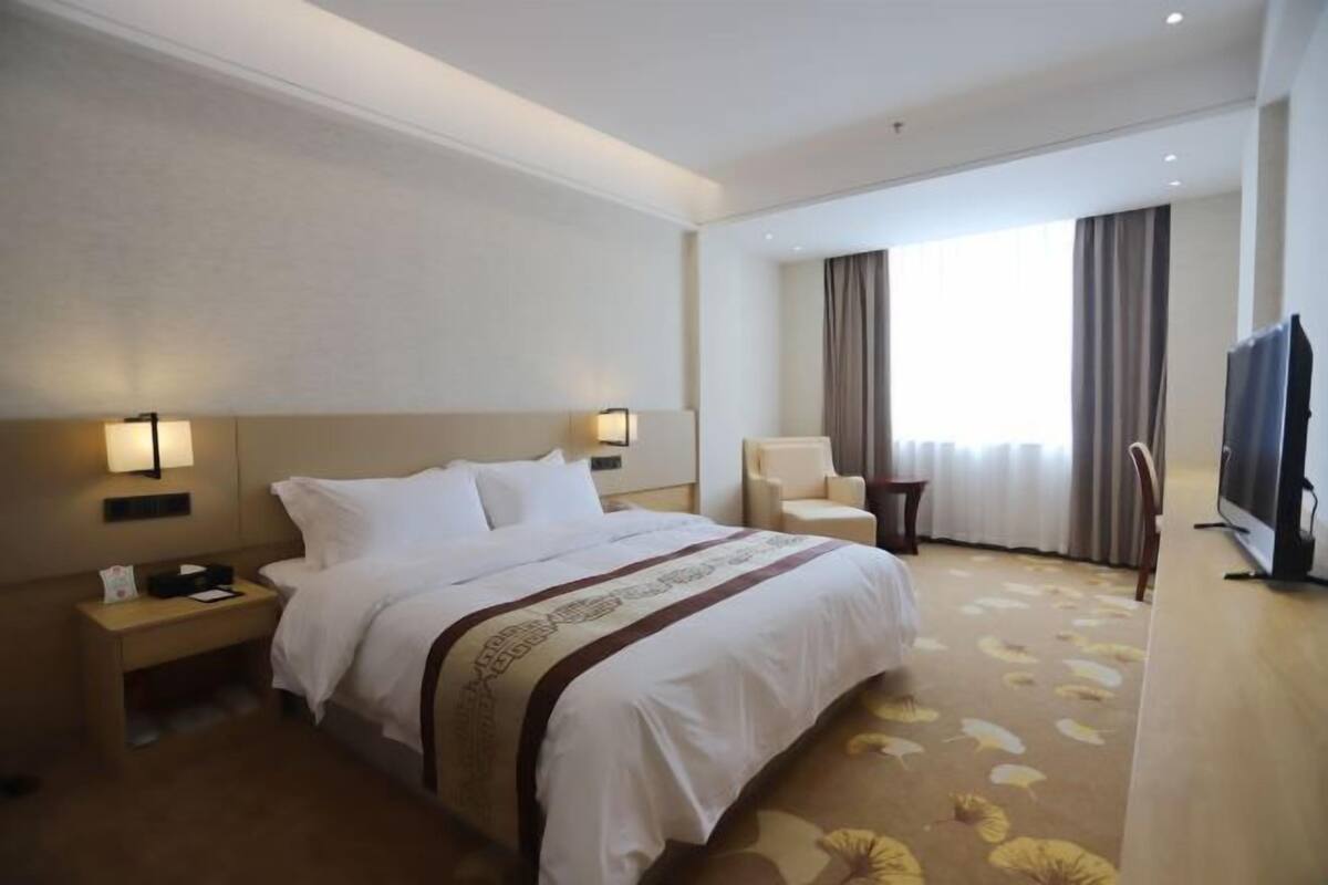 Hotelkamer met een groot bed, nachtkastjes, een stoel, een televisie en een raam met gordijnen.